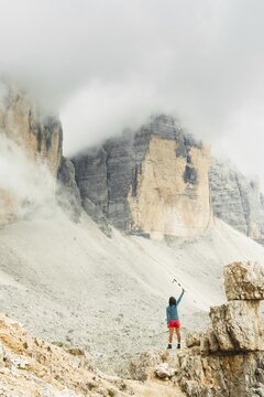 Female hiker raising trekking poles beneath misty Dolomites cliffs celebrating achievement adventure freedom and mountain exploration