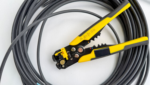 Yellow automatic wire stripper inside a loop of black electrical cable.