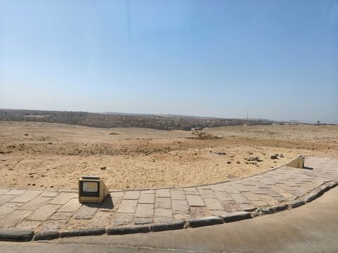 Vast Egyptian desert panorama with rolling sand dunes, rugged rocky terrain, and a clear blue sky, showcasing the dramatic beauty and serene emptiness of the arid landscape under bright sunlight.