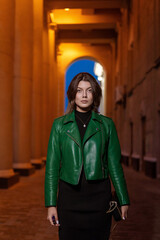 Obraz premium Stylish woman in green leather jacket posing in city night