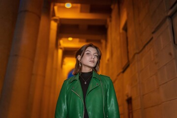 Obraz premium Stylish woman in green leather jacket posing in city night