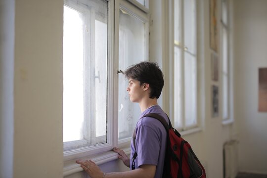 Teenage student with backpack looks out a window
