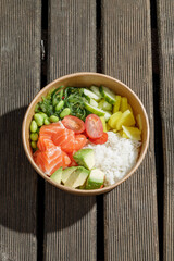 Salmon poke bowl in a delivery box on a wooden surface. Isolated © Cavan