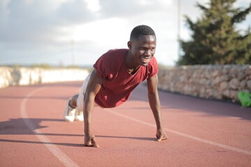 Fototapeta premium Young Black man smiling while doing pushups outdoors