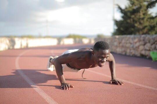 Fit Black man does a push up on a running track