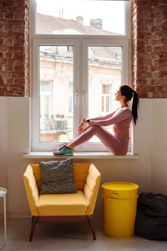Healthy and fit woman in sportswear sitting in windowsill