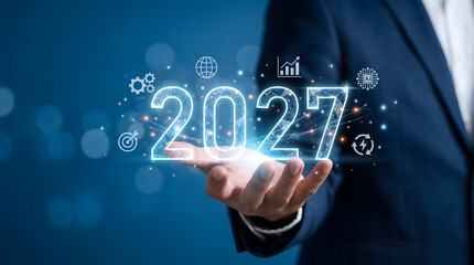 Fototapeta premium Businessman holding glowing 2027 hologram with digital network and future technology icons, new year business concept, Corporate strategy and future vision for 2027.