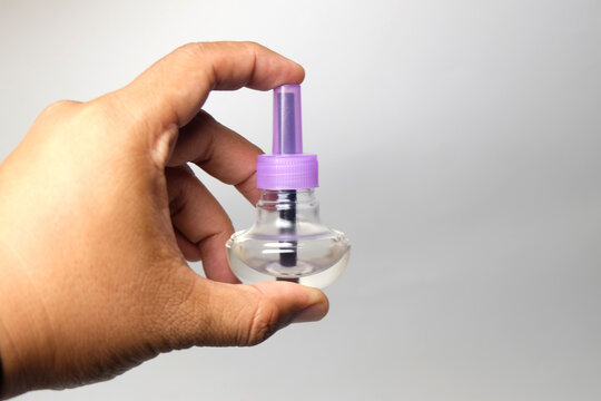 hand holding a small clear glass refill bottle with a purple plastic cap and dark wick.