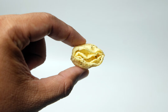 hand holding a small, hollow, crispy savory snack chip against a plain light gray background.