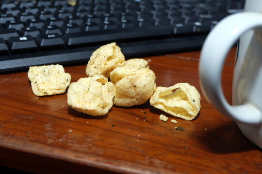 Savory crispy snacks lying on a wooden desk next to a white mug