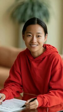 Closeup portrait of smiling young woman in red hoodie at glass table signing forms for lifestyle banner and background design