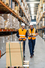 Fototapeta premium Two workers moving a large package with a pallet jack, discussing inventory and stock management in a busy distribution center
