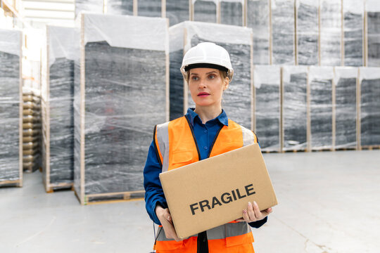 Worker in safety gear holding fragile package, managing inventory and distribution in a modern warehouse environment