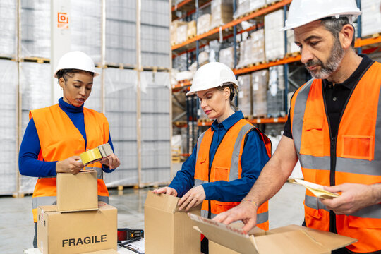 Diverse team of logistics workers wearing safety gear, preparing packages with fragile labels for shipment in a warehouse