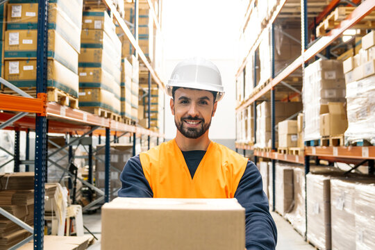 Smiling worker wearing hard hat and safety vest managing packages for distribution in a modern warehouse facility