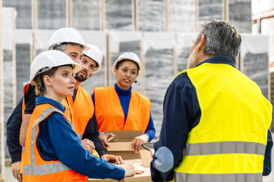 Logistics workers in safety gear listening to their supervisor giving instructions in a modern warehouse distribution center