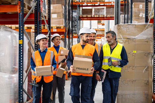 Diverse group of warehouse workers wearing safety vests, hard hats, and holding boxes, planning distribution in a logistics center