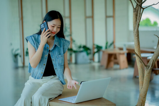 Young Asian woman reading a book with headphones and laptop by the window
