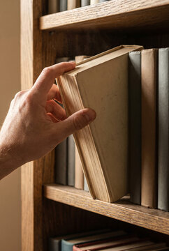 Student pulling a hardcover textbook from a library shelf