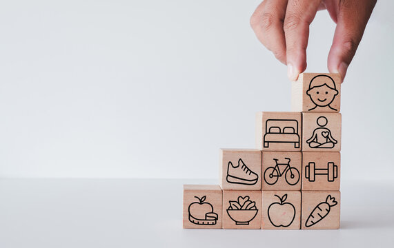 Healthy lifestyle and well-being concept. Hand stacking wooden blocks with happy face, fitness, sleep, and diet icons like stairs. Building holistic health and physical balance.