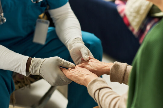 Close up of healthcare worker wearing gloves holding senior womans hands during consultation, conveying compassionate care and support. Ideal for elder care, clinic, caregiving marketing