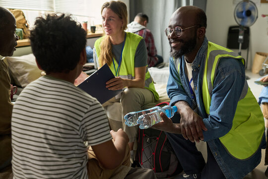 Medium shot of diverse aid workers distributing water and coordinating support with displaced adults in shelter, representing humanitarian relief. Ideal for nonprofit campaigns