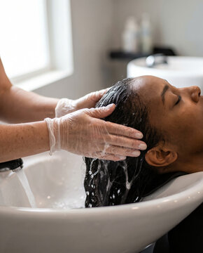 Stylist rinsing hair dye from a woman's hair at salon sink
