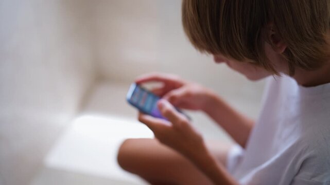 Young boy absorbed in smartphone while sitting on toilet, unable to disconnect from mobile device, representing smartphone dependency and constant digital connectivity in everyday life.