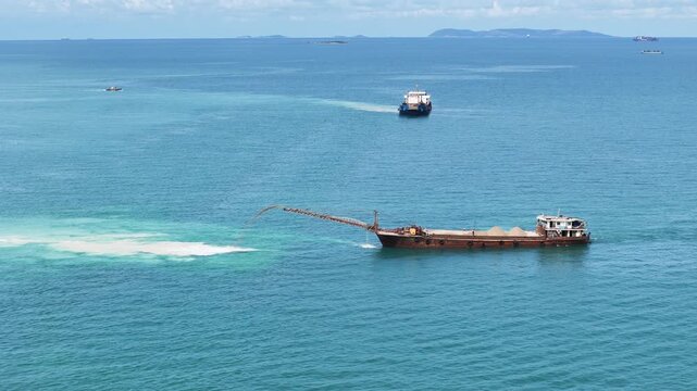 Sand dredging ship discharging sand into the sea for land reclamation project. Coastal engineering and marine infrastructure development. Industrial vessel working on artificial island construction.