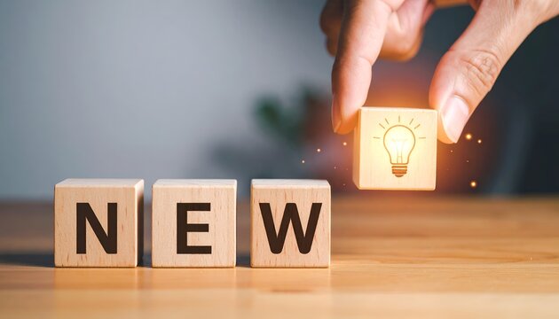 Hand positioning illuminated idea cube near NEW letter blocks, representing innovation, creativity, product launch, and modern business concepts.