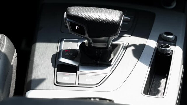 Modern automatic transmission gear shifter, car interior showing "P" for Park position, contemporary design, electronic controls, brushed aluminum accents bathed in sunlight, DSG
