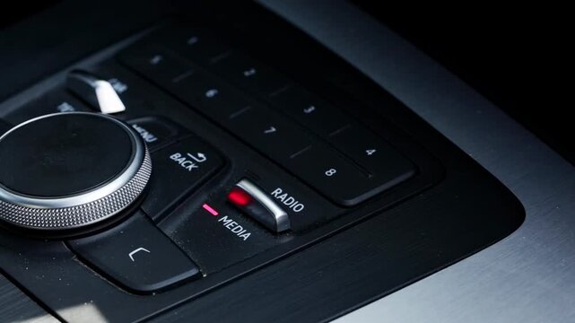 Car infotainment system central control panel with rotary dial and multiple buttons in vehicle interior, illuminated RADIO and MEDIA buttons indicate active selections of audio source
