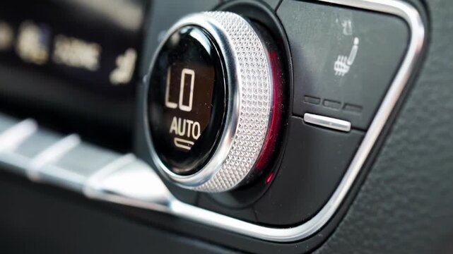 Automotive interior detail of climate control system featuring rotary knob with automatic low temperature mode display and additional controls for seat heating function.