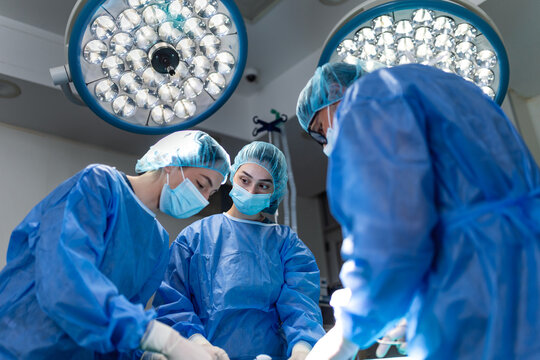 Surgeon team in action. Medical professionals performing operation, Hospital and surgery concept. Doctors wearing blue scrubs and masks working under surgical lights in the operating room.