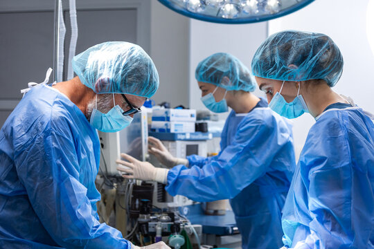 Medical team during operation. Hospital surgery concept, Professional doctors in blue scrubs and masks working in operating room. Healthcare and medicine professionals monitoring equipment.