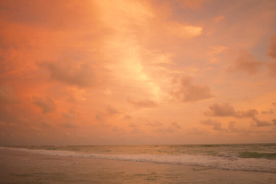 Gentle waves wash ashore under a vibrant orange sunset sky