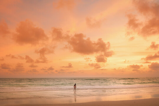 Young girl wading in the ocean during a vibrant sunset