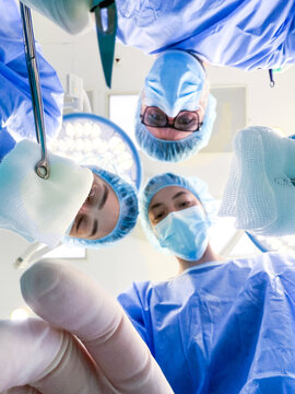 Surgeons looking down from patient perspective. Medical team performing operation in operating room, Point of view surgery concept with doctors in blue scrubs.