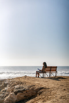 Woman enjoying solitude and relaxation reading a book by the sea