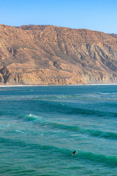 Surfer paddling surfboard on turquoise ocean in Imsouane, Morocco