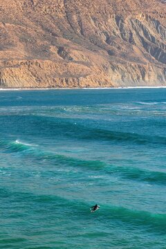 Lone surfer in vast ocean near cliffs in Imsouane, Morocco