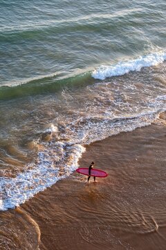 Surfer walking along the shore with a pink surfboard in Imsouane
