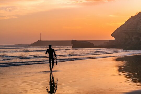 Surfer walking on Imsouane beach at golden hour sunset in Morocco
