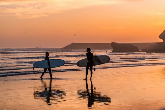 Surfers couple walking beach at sunset in Imsouane, Morocco