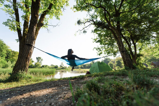 Sport girl lying on hammock on meadow near lake