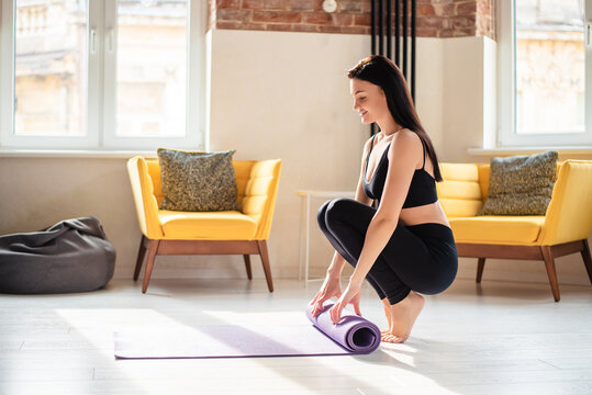 Young woman in sport clothes rolling out yoga mat