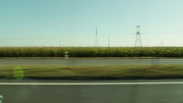 Blurred motion view from car window of highway passing rural landscape with green fields and distant electricity pylons under clear blue sky on sunny summer day travel concept, copy space for text