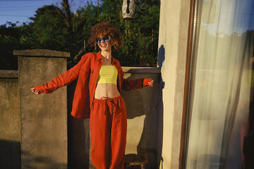 Obraz premium A woman in orange tracksuit and lime top stands outdoors, radiating casual lifestyle energy under sunny light, with a modern balcony backdrop