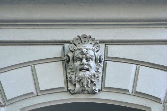 A close up shot of a detailed stone mascaron depicting a bearded face carved into the arch keystone of a historic building facade.