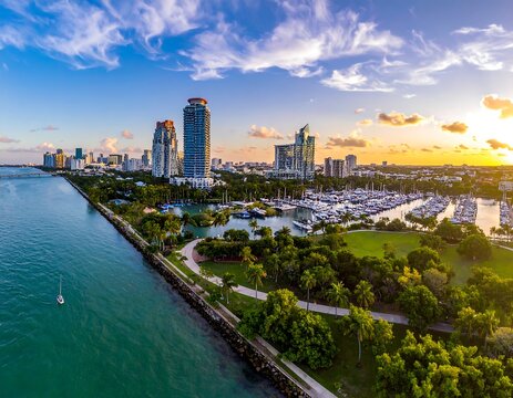 Aerial view of a city skyline at sunset, with tall buildings, a marina, green spaces, and a body of water
